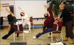 Two therapists lead and assist with stretching exercises while sitting.